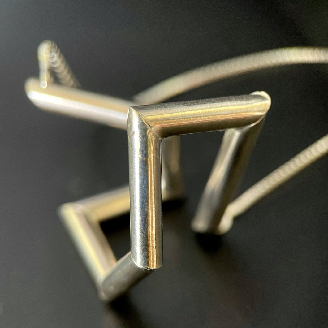 A necklace made of silver tubing that turns at sharp angles, twisting back on itself.