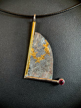 Load image into Gallery viewer, A triangular necklace, hanging at an angle. The silver has a terrain-like pattern, and is bordered on the left and bottom with wire - gold on the left, silver on the bottom. The silver wire terminates in a lab-grown ruby. The third side is a raw, curving edge. There is a branching gold pattern winding its way across the necklace.
