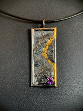 Load image into Gallery viewer, A rectangular silver necklace hanging vertically. It is framed in silver wire, and the silver has a terrain-like texture. The righthand side wire has gold near the top, which then loops in to the necklace and follows a recessed path in the silver, before looping back to the wire and running gold until the bottom. In the lower right is a lab-grown purple sapphire.
