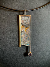 Load image into Gallery viewer, A rectangular silver necklace, handing vertically. The silver is textured in a terrain-like pattern. The necklace is framed on the top and sides in wire - gold on the left side, the rest in silver. Both side wires continue below the body of the piece, moreso on the right side, which also terminates in a lab-grown alexandrite gemstone. There are small pools of gold in some of the recessed portions of the texture.
