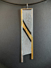 Load image into Gallery viewer, A rectangular silver necklace, hanging vertically. The silver is textured in a terrain-like pattern. There are two diagonal gaps across the body of the necklace, going from upper left to lower right. The top and sides are framed in silver wire. Starting in the upper left corner, the wire is gold, and the path of gold flows across the thin middle section between the gaps, before continuing along the bottom of the wire on the righthand side.
