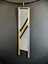 Load image into Gallery viewer, A rectangular silver necklace, hanging vertically. The silver is textured in a terrain-like pattern. There are two diagonal gaps across the body of the necklace, going from upper right to lower left. The top and sides are framed in silver wire. Starting in the upper right corner, the wire is gold, and the path of gold flows across the thin middle section between the gaps, before continuing along the bottom of the wire on the lefthand side.
