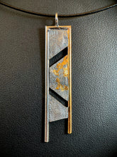 Load image into Gallery viewer, A long rectangular necklace, hanging vertically, with a terrain-like pattern in the silver. There are two gaps dividing the main body, the upper running from upper right to lower left, and then running from middle left to lower right. The necklace is framed on the top and sides with wire - gold on the right and the rest in silver. The side wires continue below the piece, longer on the silver side. There is a cascading pattern of gold in the recessed parts of the silver in the center piece.

