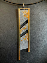 Load image into Gallery viewer, A rectangular silver necklace, hanging vertically. The silver is textured in a terrain-like pattern. The top and sides are framed in wire, with the bottom of the sides continuing below the body of the necklace, longer on the left than the right. The side wires are gold and the top is silver. There are two gaps running diagonally through the piece, from upper right to lower left. There are creeping, branching patterns of gold spreading across the silver on all three sections.
