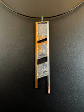 Load image into Gallery viewer, A long rectangular silver necklace. The body is textured in a terrain like pattern, and it is split into three portions, with slightly tilted gaps between them. The top and right side are framed in silver, the left in gold. The gold wire hangs below the body of the necklace, with the silver edge hanging further below that. There are branching, organic patterns of gold reaching out from around the top gap on each of the top two sections.
