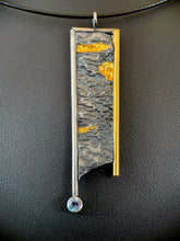 Load image into Gallery viewer, A long rectangular silver necklace. The silver is textured in a terrain-like pattern. The piece is bordered in wire on the top and sides - gold on the right, the rest in silver. Both side borders hang below the piece, longer on the silver side, which terminates in a lab-grown alexandrite. There are three thick brushes of gold in the recessed portions of the silver.

