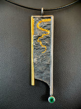 Load image into Gallery viewer, A long rectangular silver necklace. The silver is textured in a terrain-like pattern. The piece is bordered in wire on the top and sides - gold on the left, the rest in silver. Both side borders hang below the piece, longer on the silver side, which terminates in a lab-grown emerald. There is a winding gold pattern coming from the top, nestled in the recessed portions of the silver.
