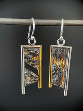 Load image into Gallery viewer, A rectangular pair of earrings, hanging vertically. The top and both sides are framed in wire - silver on the top and inside edge, gold on the outside. The silver wire on each earring hangs lower, with the gold dropping a short way below the edge of the rectangle. The center of the rectangle is reticulated silver, in a textured, terrain-like pattern. The left earring has a gap in the main portion, running diagonally from upper right to lower left. Both earrings have gold in the recessed portions.
