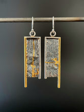 Load image into Gallery viewer, A rectangular pair of earrings, hanging vertically. The top and both sides are framed in wire - silver on the top and inside edge, gold on the outside edge. The outside border on each earring hangs lower, with the inside dropping just below the edge of the rectangle. The center of the rectangle is reticulated silver, in a textured, organic, terrain-like pattern. On the left earring there is a vertical, uneven, organic stripe of gold, which curls up again towards the right near the bottom. 
