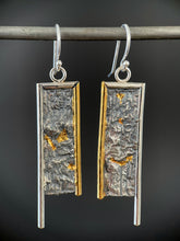 Load image into Gallery viewer, A rectangular pair of earrings, hanging vertically. The top and both sides are framed in wire - silver on the top and outside edge, gold on the inside edge. The outside border on each earring hangs lower, with the inside dropping just below the edge of the rectangle. The center of the rectangle is reticulated silver, in a textured, organic, terrain-like pattern. There are pockets of gold in some of the recessed parts.
