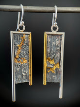 Load image into Gallery viewer, A rectangular pair of earrings, hanging vertically. The top and both sides are framed in wire - silver on the top and outside edge, gold on the inside. The silver border on each earring hangs lower, with the gold dropping just below the edge of the rectangle. The center of the rectangle is reticulated silver, in a textured, terrain-like pattern. The left earring has a hooking pattern of gold, coming from the center top down and to the right. The other has a horizontal V shape of gold in the lower half.
