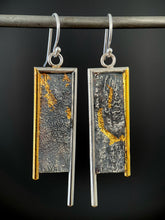 Load image into Gallery viewer, A rectangular pair of earrings, hanging vertically. The top and both sides are framed in wire - silver on the top and inside edge, gold on the outside edge. The silver border on each earring hangs lower, with the gold dropping just below the edge of the rectangle. The center of the rectangle is reticulated silver, in a textured, terrain-like pattern. There are dots of gold on the left earring, and a deep, curving line of gold on the right earring running from mid-top down and then hooking to the right.
