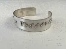 Load image into Gallery viewer, A sterling silver cuff bracelet resting on a brailled paper background. The cuff has accurately sized, spaced, and contracted braille, which in this photo reads &quot;in possibil&quot;
