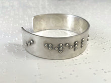 Load image into Gallery viewer, A sterling silver bracelet resting on brailled paper background. The bracelet has appropriately sized, spaced, and contracted braille, which in this photo reads &quot;I dwell&quot;
