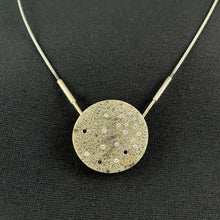 Load image into Gallery viewer, A round silver pendant. There&#39;s a scattering of small round cubic zirconia, more concentrated in the upper right and becoming more sparse in the lower left. There are three empty holes, and a droplet patter of dark oxidization on the piece.
