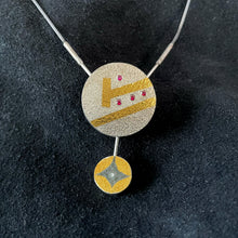 Load image into Gallery viewer, A round pendant in textured silver. There is a slanted gold line cutting across it. Above that is a line of 3 small rubies. Above that is another slanted gold line that doesn&#39;t go quite all the way across the piece, and ends in a short, perpendicular gold line. Above that is a single small ruby. Dangling from the bottom of the pendant is a smaller silver circle, with a dark 4 pointed  star in oxidized silver with the rest in gold. In the center of the darkened star is a small round moissanite stone.
