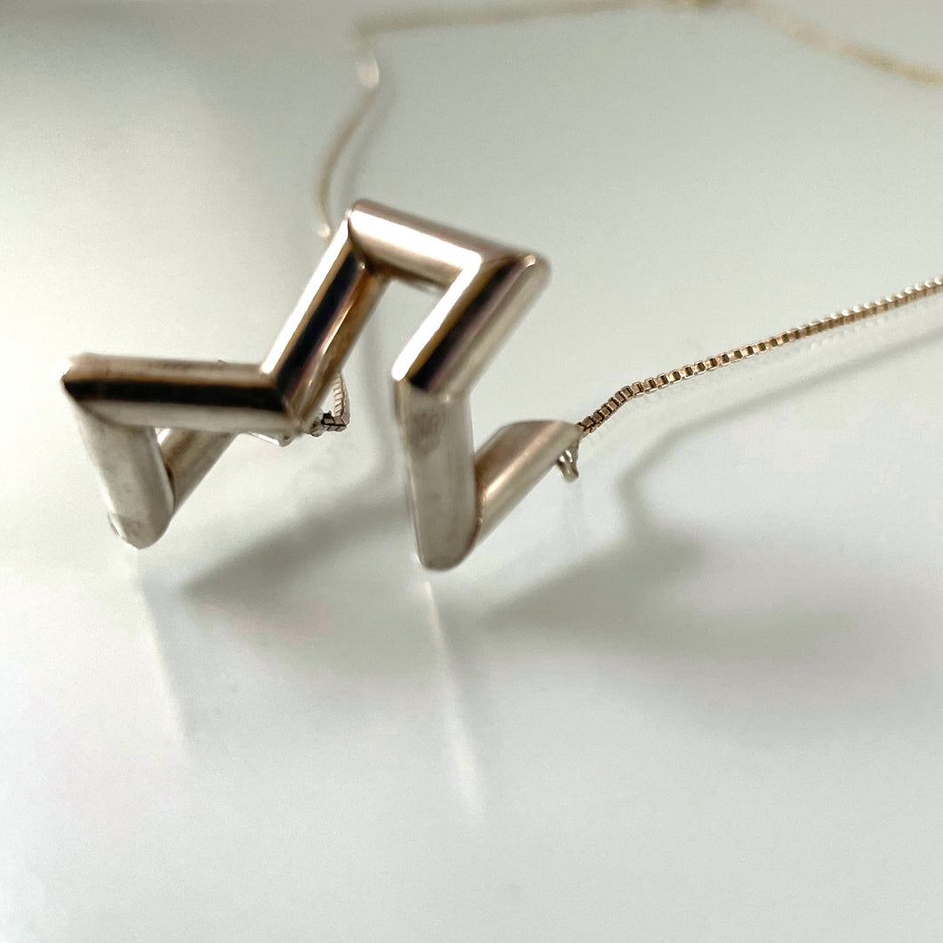 A necklace made of sterling silver tubing with sharp turns. It is vaguely U shaped, with the center of the U lifting up away from the chain connection points.