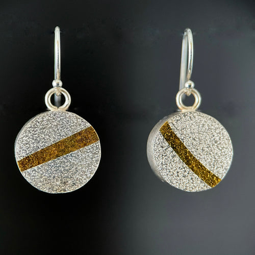 Round earrings in textured silver. There is a gold stripe across each at different angles.