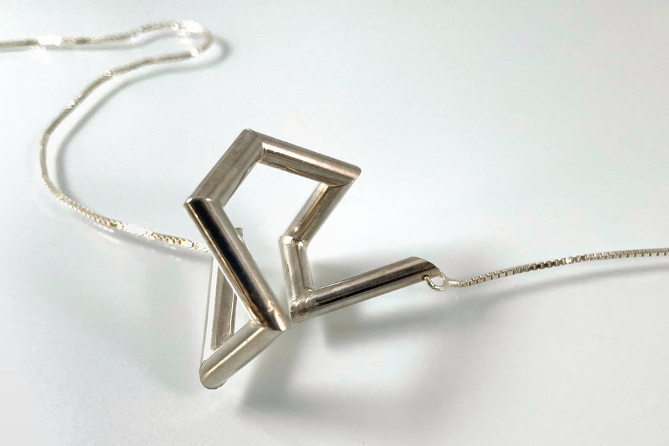 A necklace made of silver tubing that turns at sharp angles, twisting back on itself.
